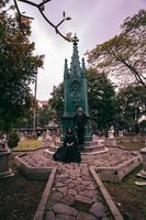 un Pareja de amantes sentado y en pie en frente de un funeral Monumento en todo negro ropa y de miedo expresiones en Víspera de Todos los Santos