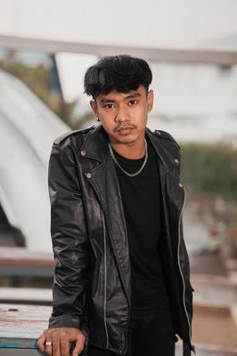 a grown man in a black leather suit and chain necklace posing very