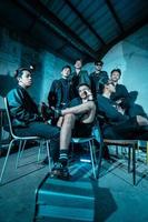 a group of Asian teenagers in black clothes posing very coolly while sitting in a warehouse chair which is lit blue photo