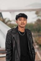 a grown man in a black leather suit and chain necklace posing very dashingly in the broad photo