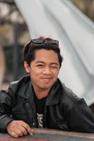 an Asian man with a chubby face wearing sunglasses and a black leather jacket while sitting at a cafe table photo