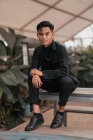 an asian boy in a black denim jacket posing like a naughty boy with a chain around his neck in a park photo