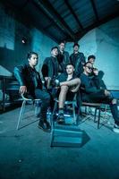 a group of Asian teenagers in black clothes posing very coolly while sitting in a warehouse chair which is lit blue photo