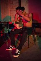 a gay man in sunglasses and denim pants sits relaxing in a club to celebrate photo