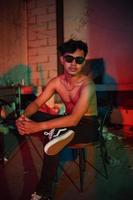 a gay man in sunglasses and denim pants sits relaxing in a club to celebrate photo