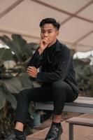 an asian boy in a black denim jacket posing like a naughty boy with a chain around his neck in a park photo