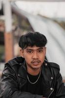 an Asian man with a naughty face wearing a chain necklace and a black leather jacket in a cafe photo