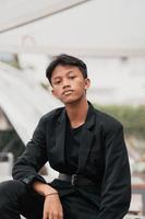 an Asian teenager in a black denim jacket posing by sitting on a cafe chair and relaxing photo