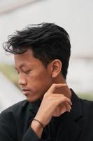 an Asian teenager in a black denim jacket leans against a garden table while relaxing and enjoying the view photo