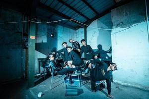 a group of Asian teenagers in black clothes posing very coolly while sitting in a warehouse chair which is lit blue photo