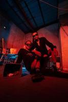 a couple of gay teenagers are sitting together wearing sunglasses and posing naughty in a warehouse with a red light photo