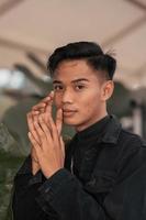 an Asian man in a black denim jacket posing with a cheerful face and very handsome in a cafe photo