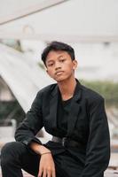 an Asian teenager in a black denim jacket posing by sitting on a cafe chair and relaxing photo