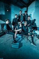 a group of Asian teenagers in black clothes posing very coolly while sitting in a warehouse chair which is lit blue photo