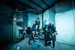 a group of Asian teenagers in black clothes posing very coolly while sitting in a warehouse chair which is lit blue photo