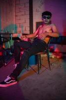 a gay man in sunglasses and denim pants sits relaxing in a club to celebrate photo