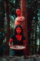 un asiático mujer y hombre fueron en pie en frente de un árbol mientras caza un animal en el medio de el bosque Hasta que ellos fueron cubierto en sangre foto