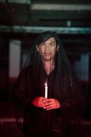 a male devil worshiper with a transparent veil is performing a spooky ritual by holding a candle in his hand photo