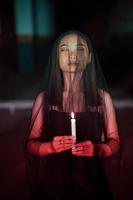 a female devil worshiper with a transparent veil is performing a spooky ritual by holding a candle in her hand photo