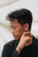 an Asian teenager in a black denim jacket leans against a garden table while relaxing and enjoying the view photo