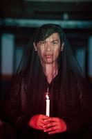 a male devil worshiper with a transparent veil is performing a spooky ritual by holding a candle in his hand photo