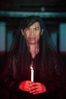 a male devil worshiper with a transparent veil is performing a spooky ritual by holding a candle in his hand photo