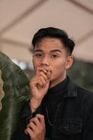 an Asian man in a black denim jacket posing with a cheerful face and very handsome in a cafe photo