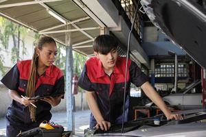 dos profesional automotor mecánico socios cheque y reparar un ev coche batería y híbrido motor a un mantenimiento cochera, experto eléctrico vehículo servicio, y fijación ocupaciones auto industria. foto