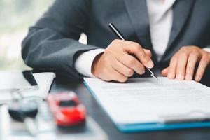 Car dealer business woman signing car insurance document or lease paper. Planning to manage transportation finance costs. Concept of car insurance business, saving buy with tax and loan for new car. photo