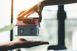 Business woman holding home miniature in office bureau. insurance protective hand over house for protection and care, Concept of home and real estate Property insurance. photo