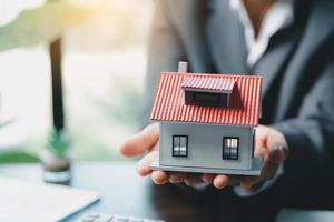 Business woman holding home miniature in office bureau. insurance protective hand over house for protection and care, Concept of home and real estate Property insurance. photo