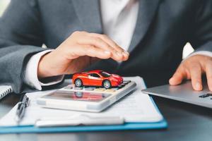 Business woman's hand protecting red toy car on desk. Planning to manage transportation finance costs. Concept of car insurance business, saving buy - sale with tax and loan for new car. photo