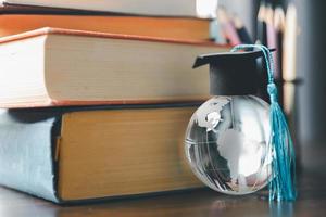 graduado estudiar extranjero programa concepto negro graduación gorra en un globo mapa y libros, representa conocimiento lata ser aprendió en línea en cualquier sitio y en todos lados, incluso en universidades o instalaciones foto