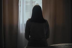 silueta de un joven mujer en pijama en contra el antecedentes de un ventana a hogar en un cama con estacional afectivo trastorno o depresión. el concepto de invierno depresión debido a carencia de luz de sol foto