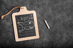 Conceptual image of the calendar day April 1 with an empty space for text on a dark background in the form of a note on the board and an image of a fish photo