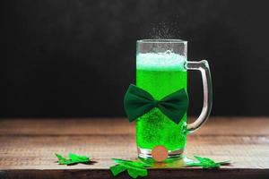 St. Patrick's day celebration, traditional green drink and clover leaves with coin on wooden background, copy space. photo