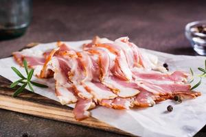 Raw smoked bacon and rosemary on a cutting board on the table. Hearty snack. photo