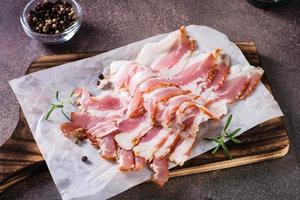 Raw bacon slices on paper on a cutting board on the table. Hearty snack. photo