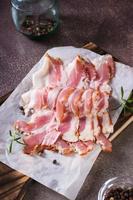 Raw bacon slices on paper on a cutting board on the table. Hearty snack. Vertical view photo
