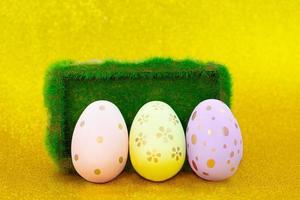 Painted eggs with pedestal with grass on yellow shiny background. Easter. Copy space photo