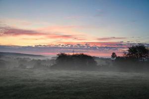 Sunrise over a neighboring forest with meadow in the foreground. Pasture landscape photo