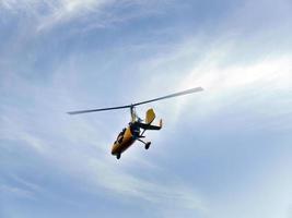 Low angle view of yellow color Gyrocopter flying in the blue sky and dramatic clouds, fun fly, aero sports, skydive, Roto craft, Gyroplane, skydiving, auto Gyro photo