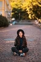 Young woman in hat sitting at city on cobblestone photo