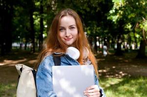 Red haired university girl with backpack and laptop smiling at camera.Back to school concept. photo