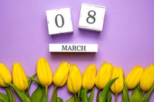 hermosa amarillo tulipanes y calendario en pastel púrpura antecedentes. concepto De las mujeres día, marzo 8. plano laico foto