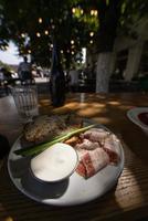 vista de cerca rebanadas de carne de tocino ahumado con pan negro integral de centeno, cebolla verde y crema agria en la mesa. foto