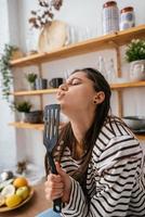 Funny woman singing into spatula, holding spatula as microphone. photo