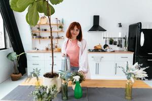 Young woman pouring water in flower pot with indoor houseplant from watering can. photo