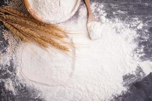 Heaps of wheat flour with ears of wheat on the table, black background - top view photo