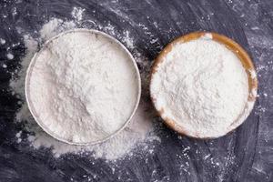 Flour in a bowl and wheat flour on table, black background In a rustic kitchen, top view photo